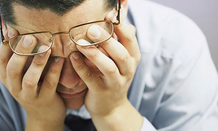 Người đàn ông đeo kính ôm đầu vì đau đớn khó chịu