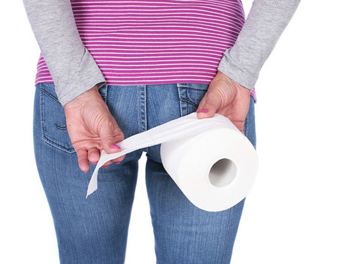 Người phụ nữ cầm cuộn giấy vệ sinh sau lưng, minh họa tình trạng táo bón